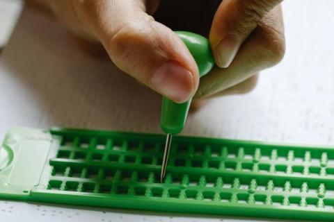 mano che scrive in braille con lo stilo e la tavoletta braille